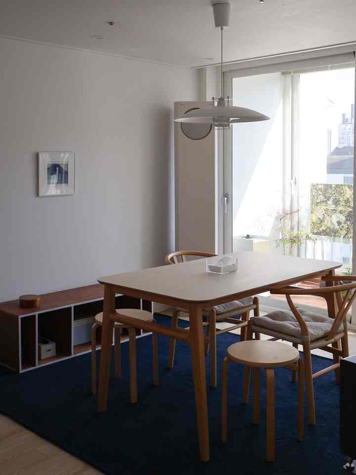 White walls, navy rug, and natural wood dining table with chairs in a bright dining room