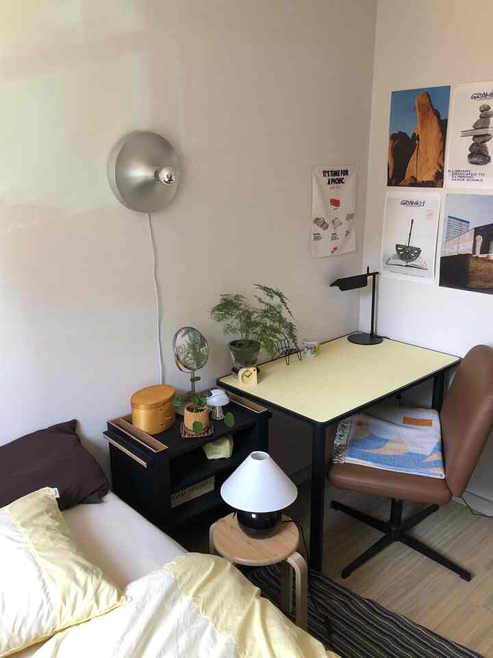 黄色と茶色がアクセントのワンルーム寝室兼ホームオフィス、ミッドセンチュリーモダン家具と壁照明が配置された雰囲気のあるインテリア