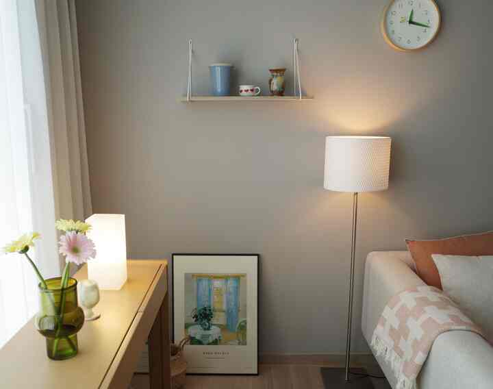 柔らかなベージュ色調のリビング、ソファ、フロアランプ、壁の棚と花瓶が配置された雰囲気のあるインテリア