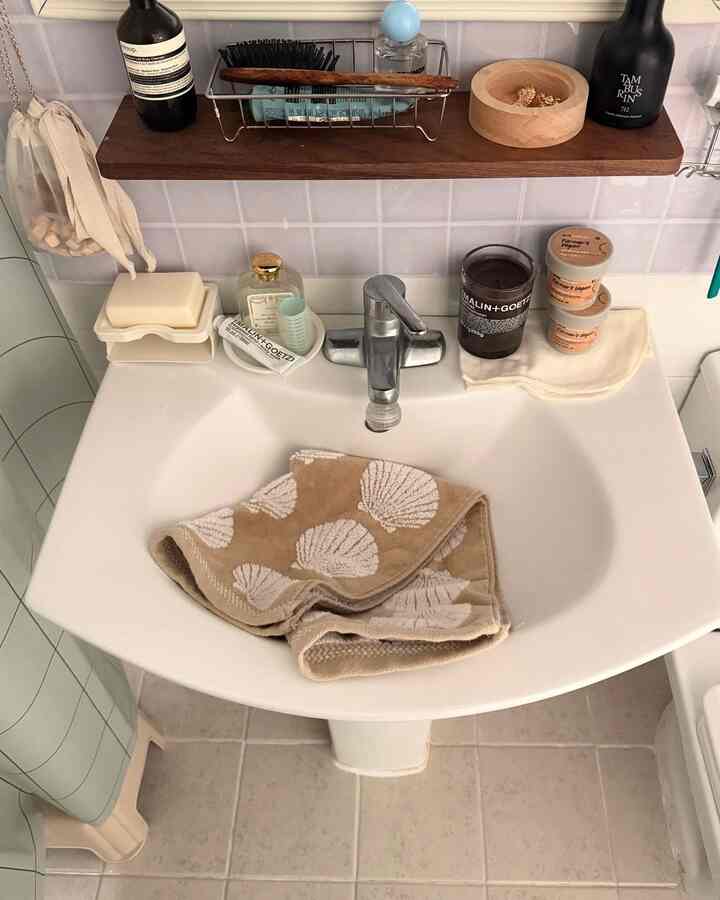 ナチュラルトーンのバスルーム洗面台、貝殻模様のタオルと木製棚が配置された清潔感のある温かみのあるインテリア