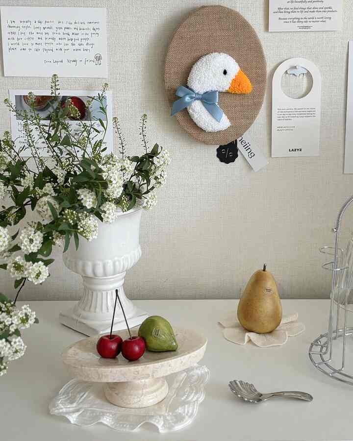 ナチュラルカラーのダイニングテーブルに大理石のフルーツオブジェ、白い花瓶、かわいい白鳥のウォールデコが配置された雰囲気のあるインテリア