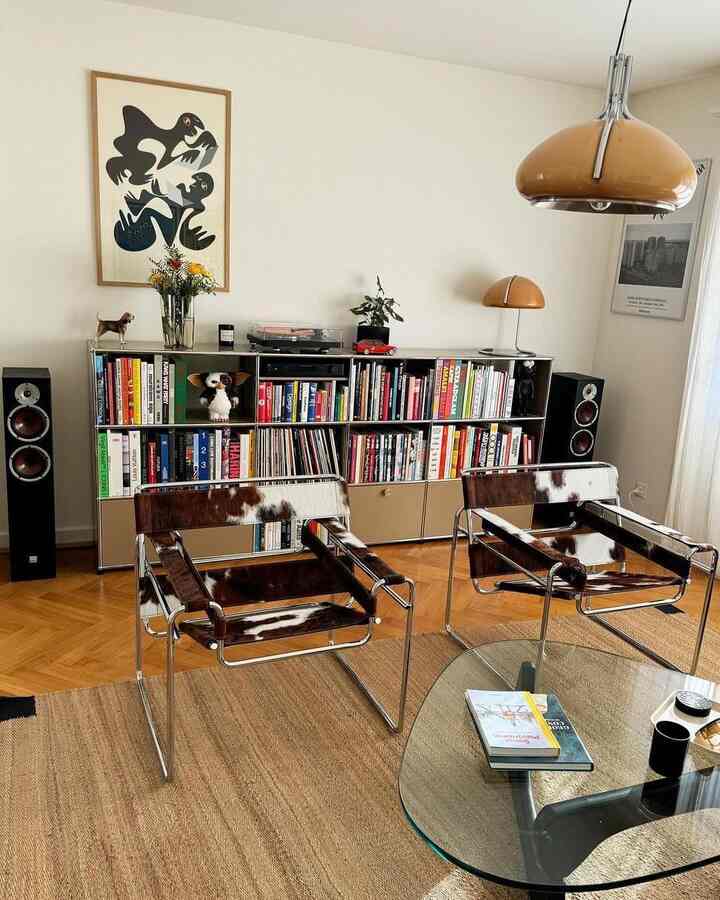 Mid-century modern living room with brown wood tones and white walls, featuring two cowhide armchairs and a glass coffee table in a cozy setting