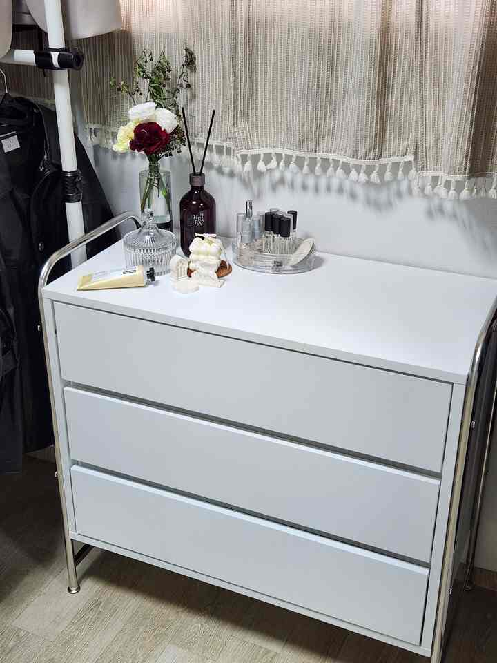 白とシルバーのトーンのウォークインクローゼット用三段チェストと小さなインテリア雑貨がある清潔な空間