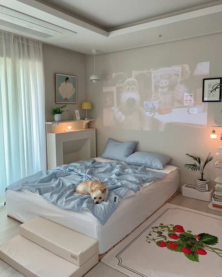 柔らかなブルーとホワイトの色調の寝室、中央にベッドと寝具が配置され、小さな犬がベッドにくつろいでいる、自然で落ち着いた雰囲気のインテリア