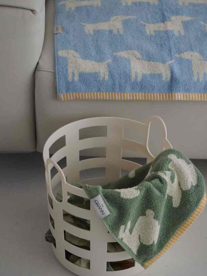 Calm indoor space featuring a white sofa, a white basket, and blue and green animal-patterned towels prominently displayed