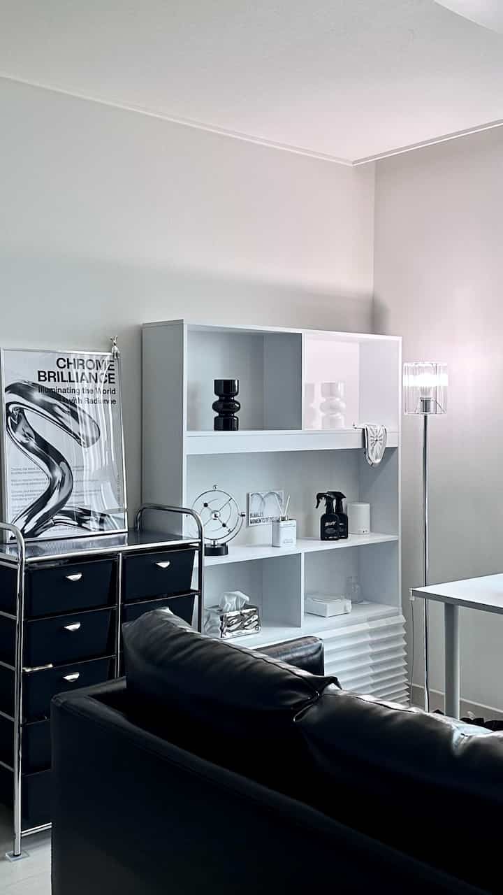 ブラックとホワイトのトーンのワンルームリビング、ホワイトの棚と黒いソファが配置されたモダンで清潔感のある空間