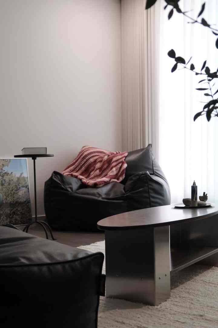 明るい白の色調のリビング、中央に黒いビーズクッションスツールとコーヒーテーブルが配置されたモダンで落ち着いたインテリア