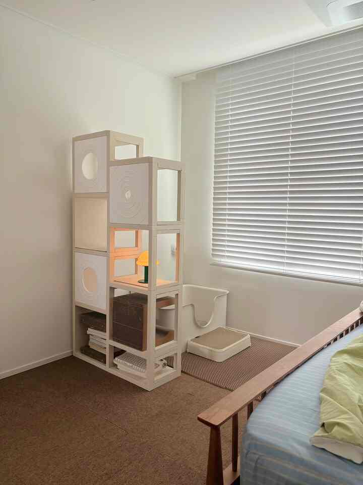 ベージュの床と白い壁のモダンな寝室に、モジュラー式のキャットタワーと猫用トイレが配置された雰囲気のあるインテリア