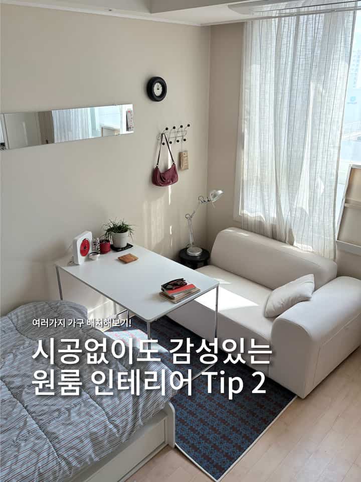 A cozy and simple studio apartment with white and beige tones, featuring a bed, sofa, and desk neatly arranged