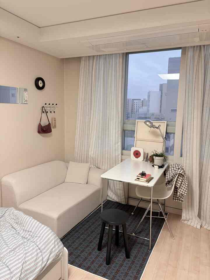 Bright beige-toned compact living room featuring white sofa and white desk lined up by the window in a practical setup