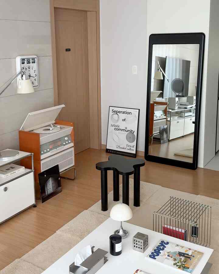 A white and wood-tone living room featuring a coffee table, black stool, and large mirror creating a cozy atmosphere