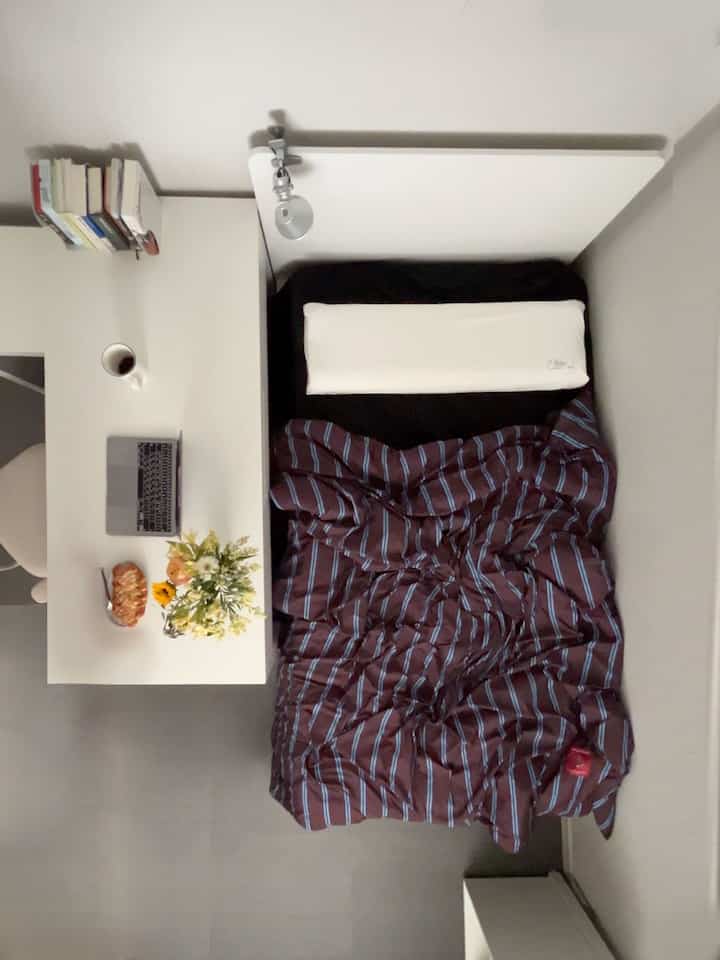White-toned studio bedroom featuring a bed with a side desk for efficient and cozy space use
