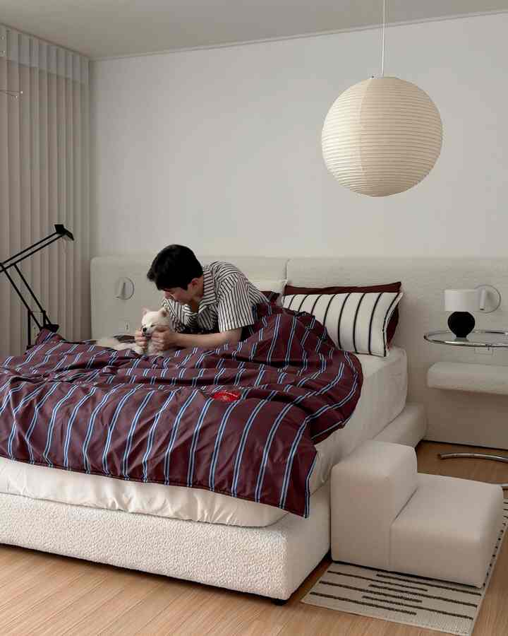 ホワイトとブラウンのトーンの寝室、中央にベッドとペットの犬、ウッドフロアが調和した印象的な空間