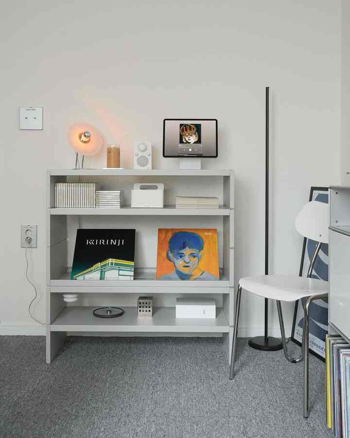 グレーのカーペットと白い壁が調和したモダンな部屋、メタル製の棚にオブジェとレコードが整然と並ぶ印象的なインテリア