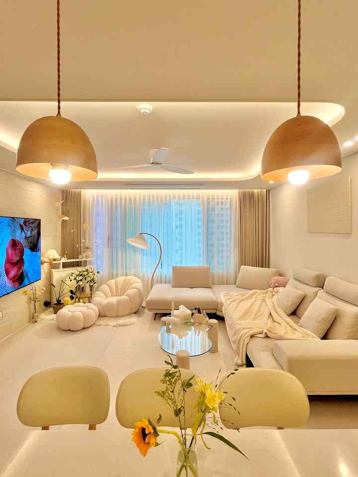 Cozy living room in warm white and beige tones featuring large sofa and wooden pendant lights with a comforting atmosphere