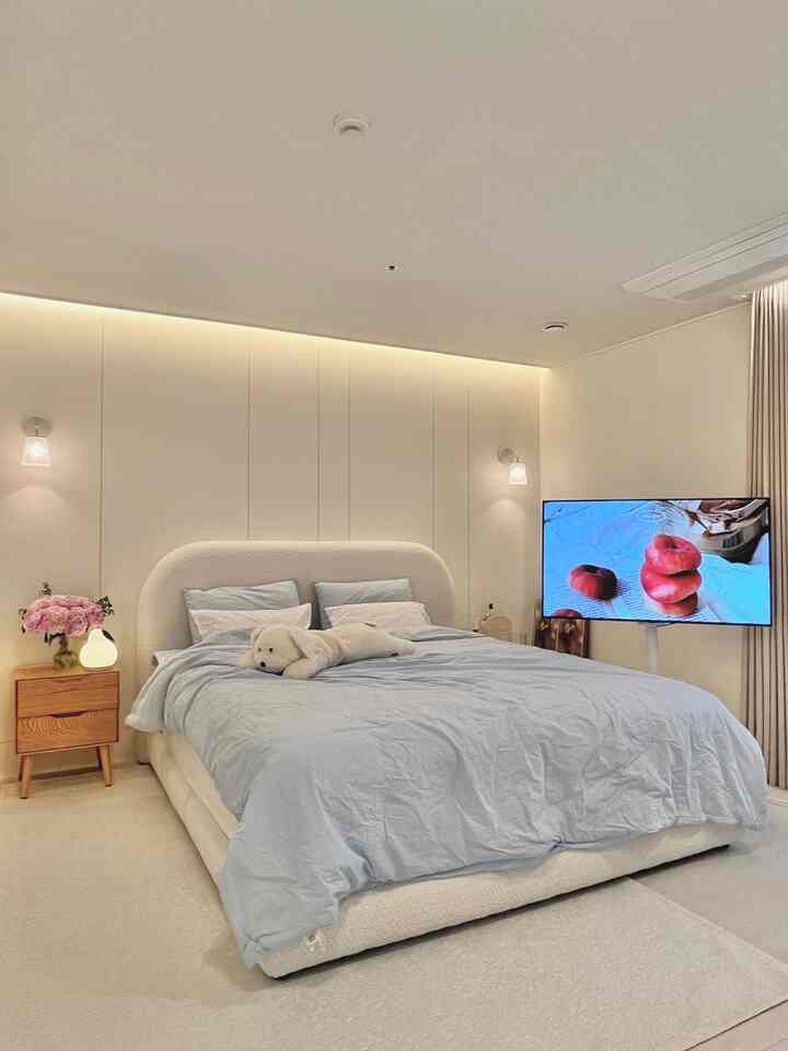 White and beige toned hotel-like bedroom featuring a cozy bed, wall sconces, and a clean, spacious atmosphere