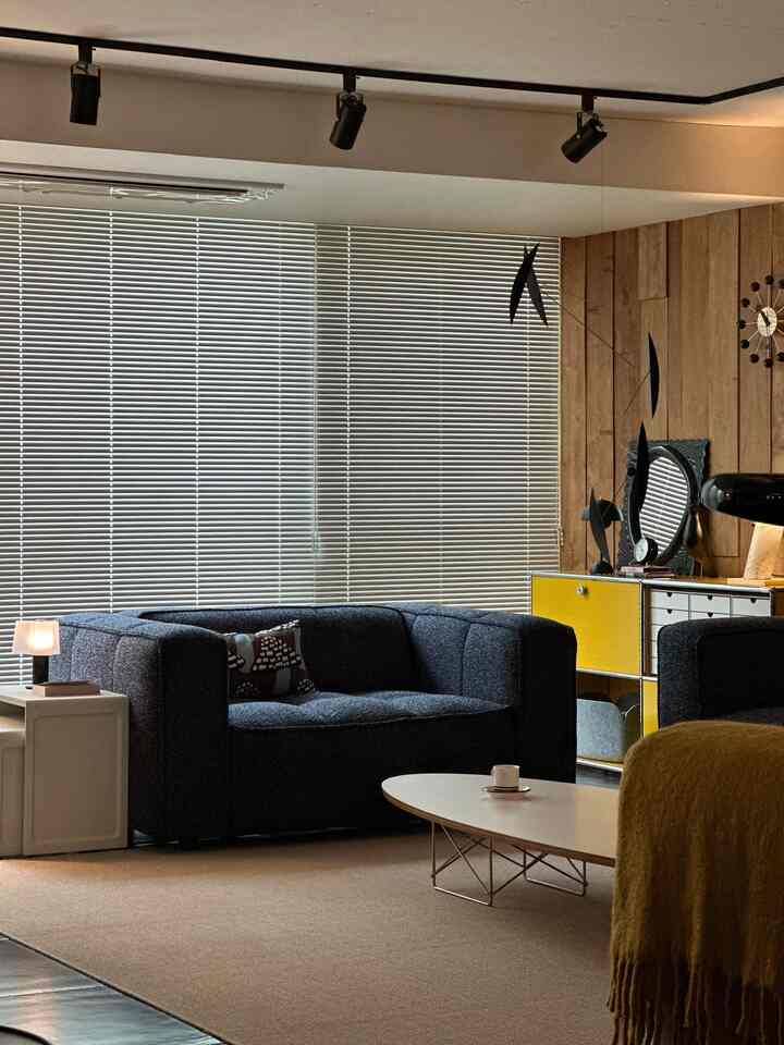 Mid-century modern living room with wood tones, black sofa, and yellow sideboard featuring blinds and stylish furnishings