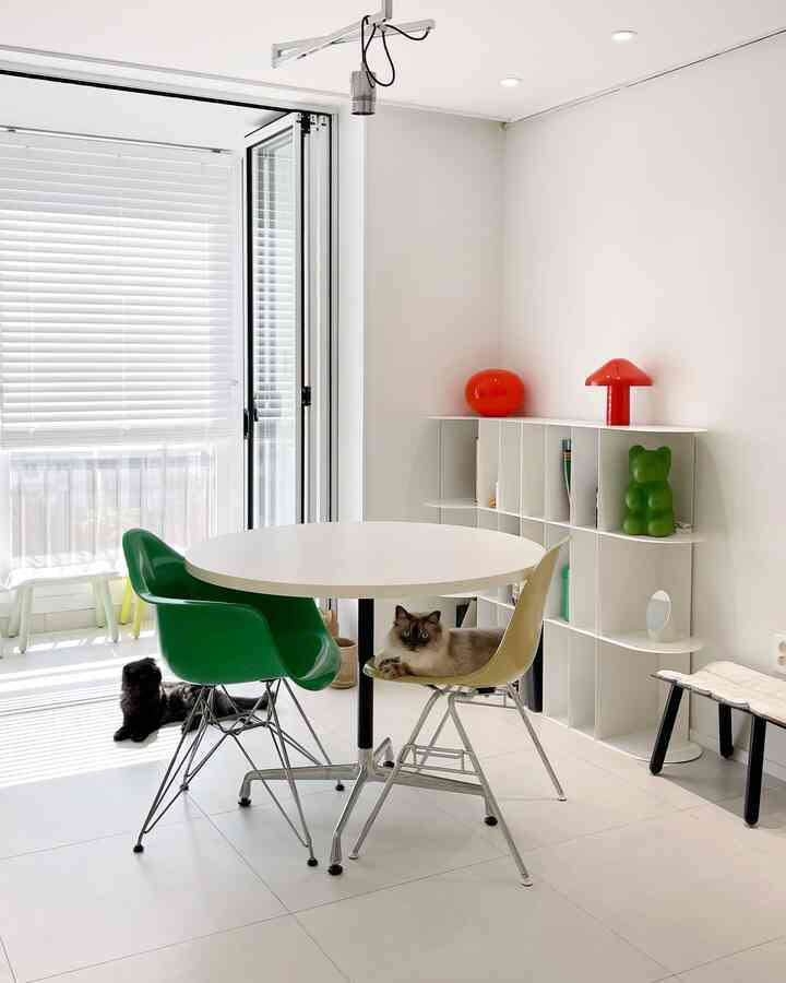 Bright white-toned living room featuring a round dining table with Eames chairs and two cats in a cozy setting