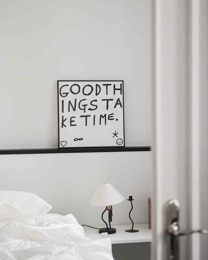 White and monotone bedroom featuring a bed with bedside table, unique framed poster, and modern lamp in a clean minimal interior