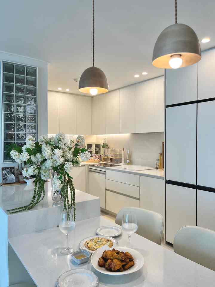 白を基調としたキッチン、アイランドテーブルとペンダントライトが配された清潔感のあるモダンな新婚の家のキッチン空間