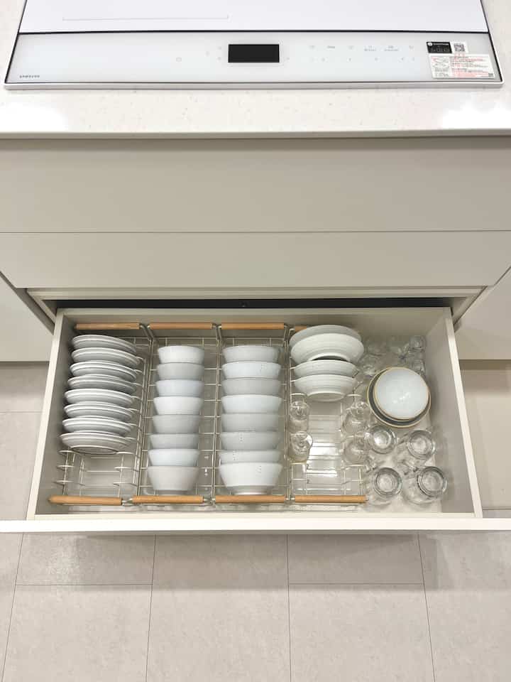 白を基調としたキッチンの引き出しに、食器や皿の収納ラックとグラスが整然と並べられたモダンなキッチンスペース