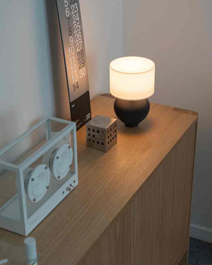温かみのある木目調のサイドボードにテーブルランプとカレンダーが配置されたミニマルで落ち着いた玄関のインテリア