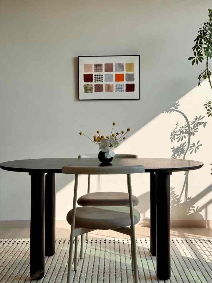 ブラックの楕円形木製ダイニングテーブルとベージュの椅子が配置されたナチュラルなダイニングルーム、壁に多彩な色のアートが飾られた雰囲気のあるインテリア