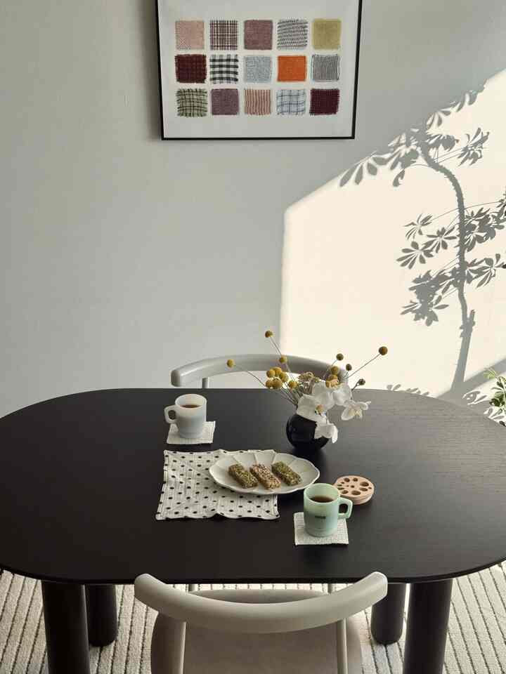 ミニマルでシンプルな雰囲気のダイニングルーム、黒いダイニングテーブルと薄いグレーのダイニングチェアが配置され、白い壁と自然光が空間を明るくしています。