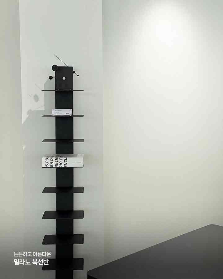 白い壁と黒のミラノ本棚が配置されたミニマルでモダンなインテリア