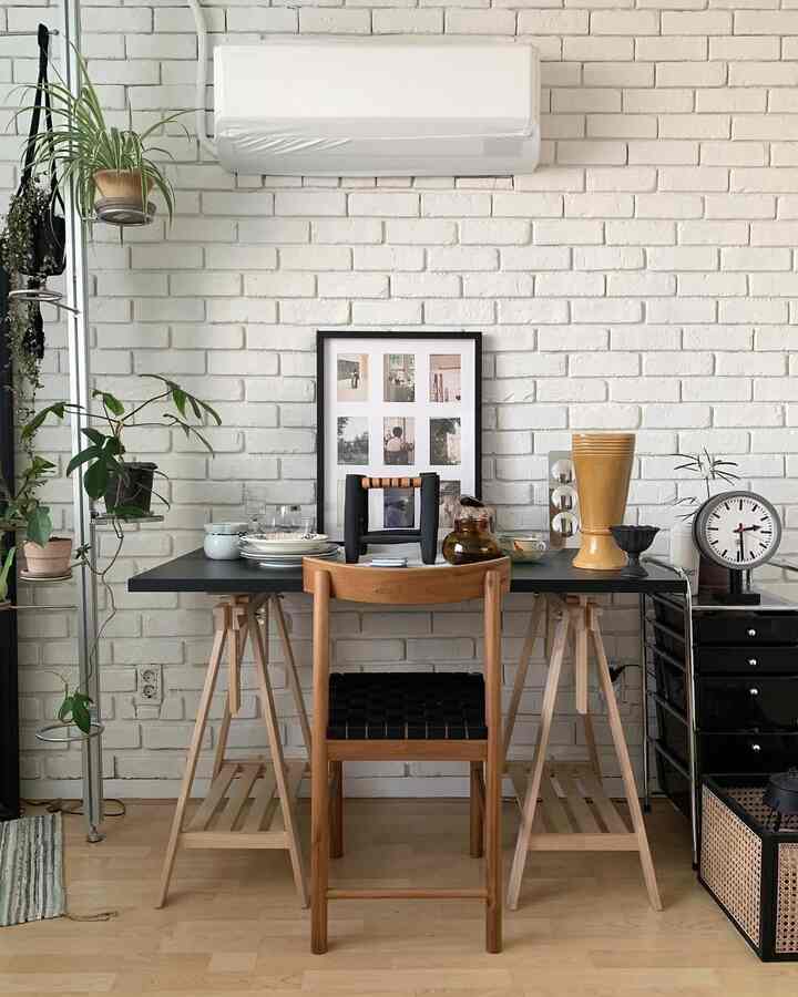 白いレンガ壁と木目調家具が調和するワンルーム、ナチュラルモダンなデスクとダイニングチェアが配置された心地よいワークスペース