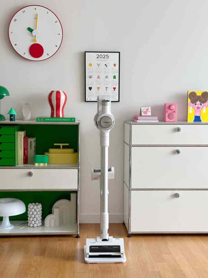 白と緑の色調のリビングルーム、中央に白いコードレス掃除機、左右に収納棚とチェストが配置された整った空間