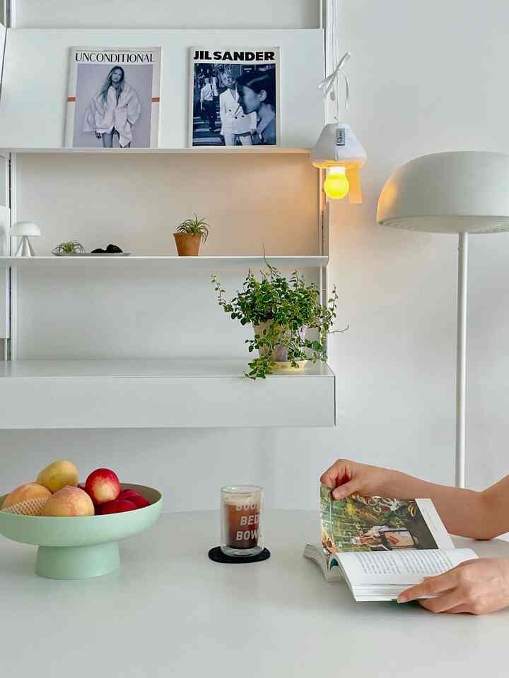 White-based kitchen and living room interior with a minimal dining table, fruit tray, and mushroom table lamp creating a cozy atmosphere