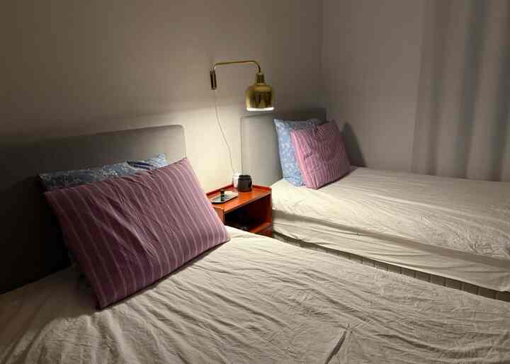 グレー調の寝室、2つのベッドとゴールドの壁掛け照明が配置されたミニマルで暖かみのあるインテリア