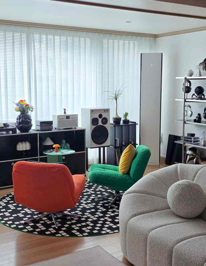 自然光が差し込むリビング、グリーンとオレンジのファブリックアームチェアとアイボリーの曲線ソファが配置されたインテリア