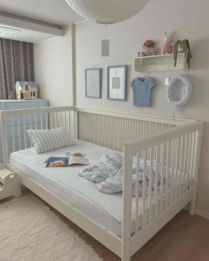 明るく爽やかなホワイトとパステルブルーの赤ちゃん部屋、白いベビーベッドとチェストが配置された温かみのある空間