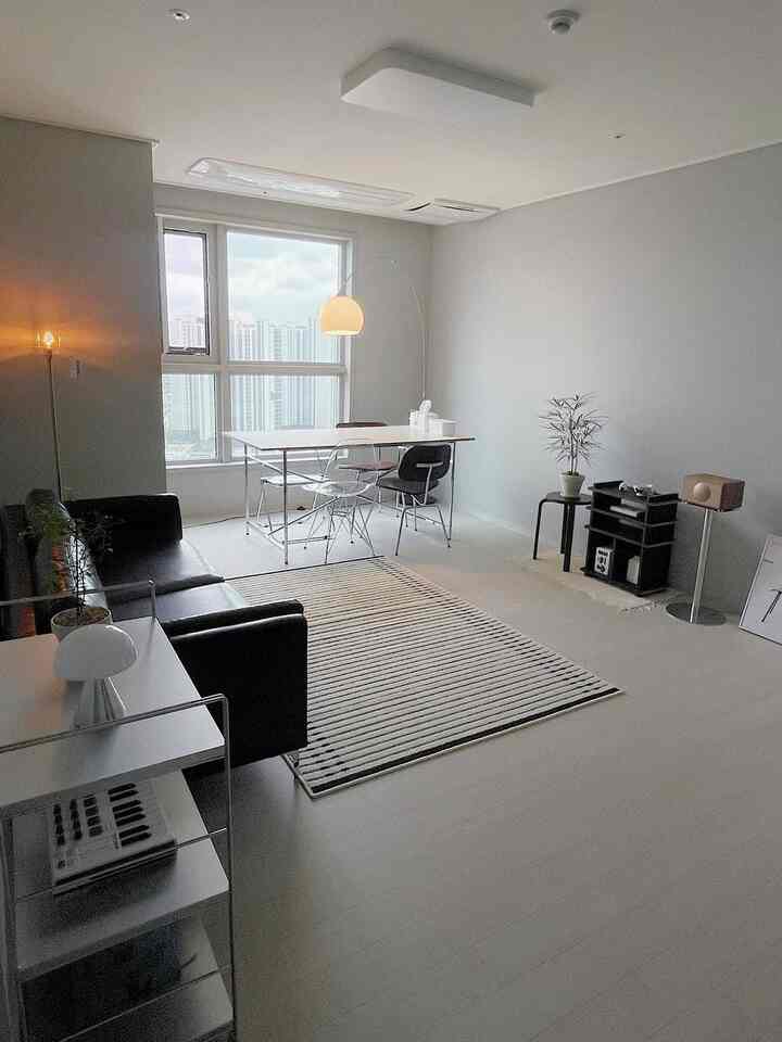 Bright white-toned living room featuring black sofa, simple dining table, and floor lamp in a modern, clean setting