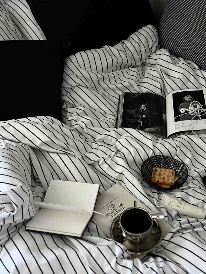 Monotone bedroom in black and white stripes, featuring bed with pillows, duvet, books, and coffee cup in a cozy setting