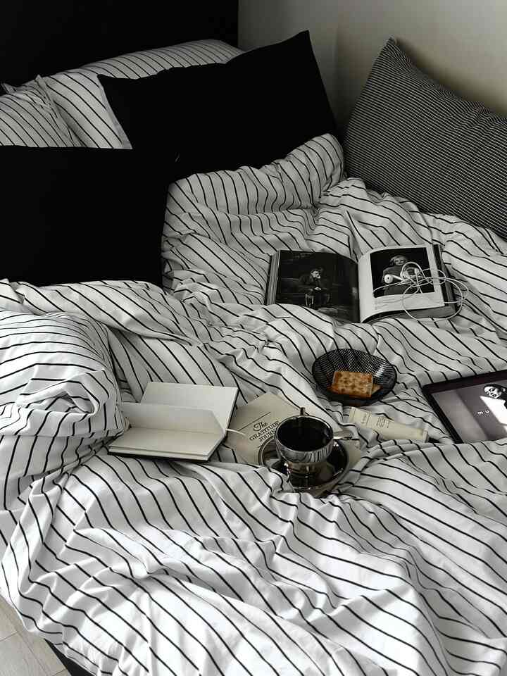 Monotone bedroom featuring a striped duvet and black pillows on a bed with coffee and books creating a cozy atmosphere