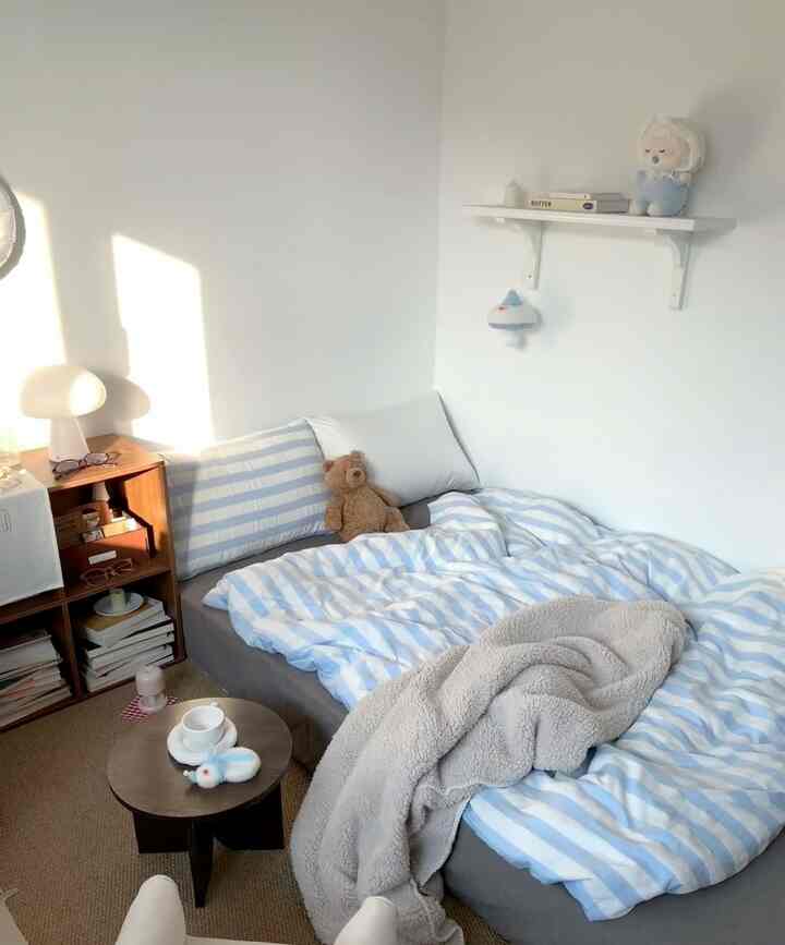 Small bedroom with white and light blue tones, featuring a simple natural-style bed and nightstand creating a cozy atmosphere