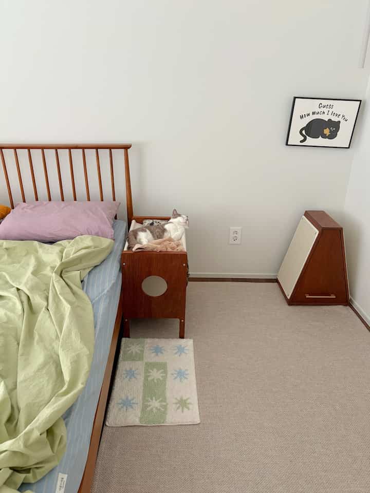 A cozy bedroom with natural wood tone furniture and beige rugs, featuring a cat resting comfortably in a wooden cat hammock