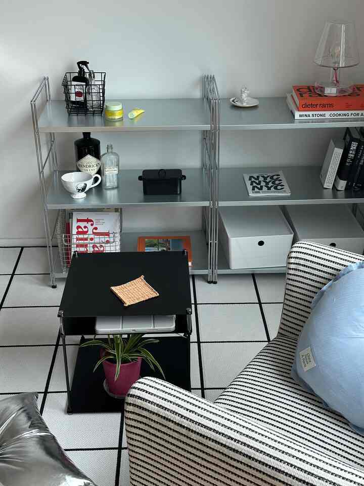 シンプルでモダンなリビング、シルバーのメタル棚と黒いコーヒーテーブル、青いクッションのアームチェアが配置された空間