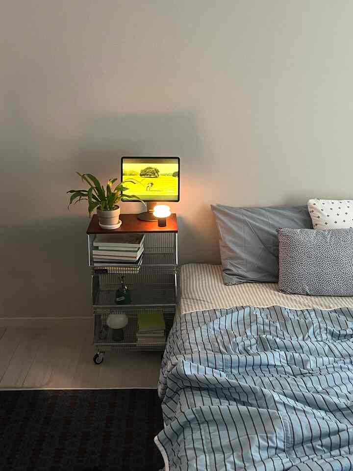 白い壁とブルーストライプの寝具がある居心地の良い寝室、左側にナイトテーブルとランプ、植物が配置された空間