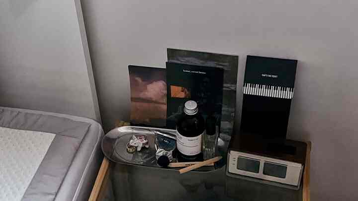 白と木目調が調和したサイドテーブルの上にレトロなデジタル時計と香りの製品が置かれたモダンな寝室のインテリア