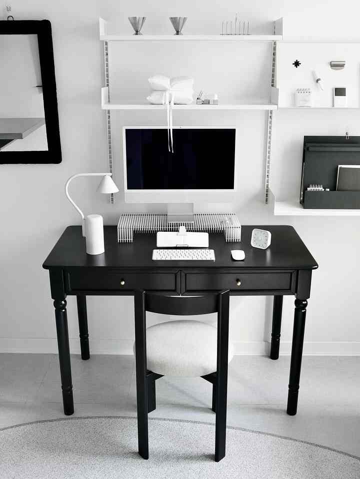 Monotone home office space featuring a black desk, chair, computer monitor, and desk lamp arranged neatly at center
