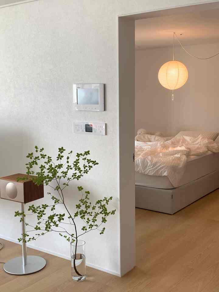 ナチュラルな木目調の床と白い壁、寝具が配されたモダンな寝室、透明な花瓶に枝が挿されている