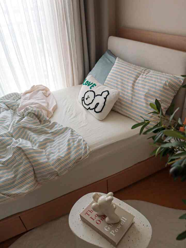 ナチュラルなベージュの子供部屋、シングルの木製ファブリックベッドとストライプの寝具が配置された落ち着いた雰囲気の寝室