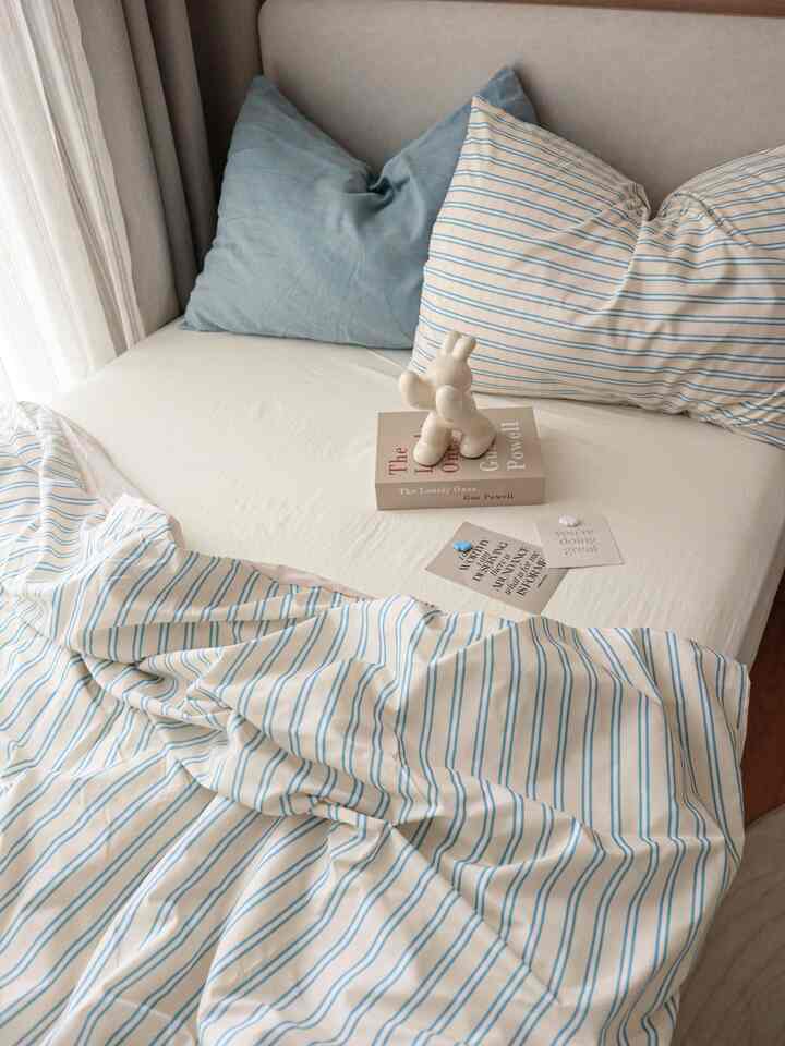 ベージュとホワイトの色調の子供部屋、シングルベッドに青のストライプ寝具と枕が配置された雰囲気のある空間