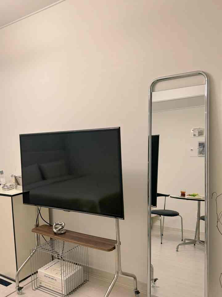 ベージュ調の壁と床、シルバーのフレームの全身鏡と木製棚のテレビ台が配置されたヴィンテージ感のあるワンルームのリビング