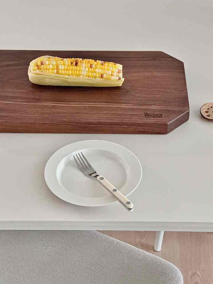 白いセラミックテーブルに茶色い木製まな板と黄色の焼きとうもろこしが置かれたシンプルなキッチン