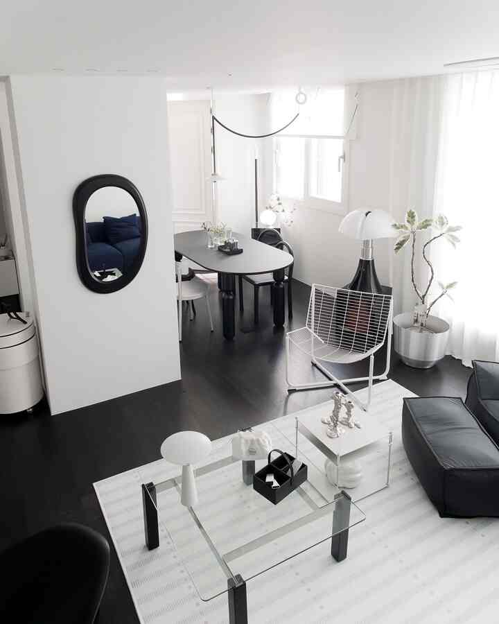 A modern and simple living and dining space in white and black tones featuring a black dining table, sofa, glass coffee table, and table lamps